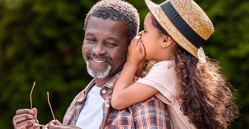 Girl whispers into her father’s ear at a park