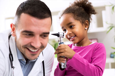 Smiling little girl looking in doctors ear using an otoscope