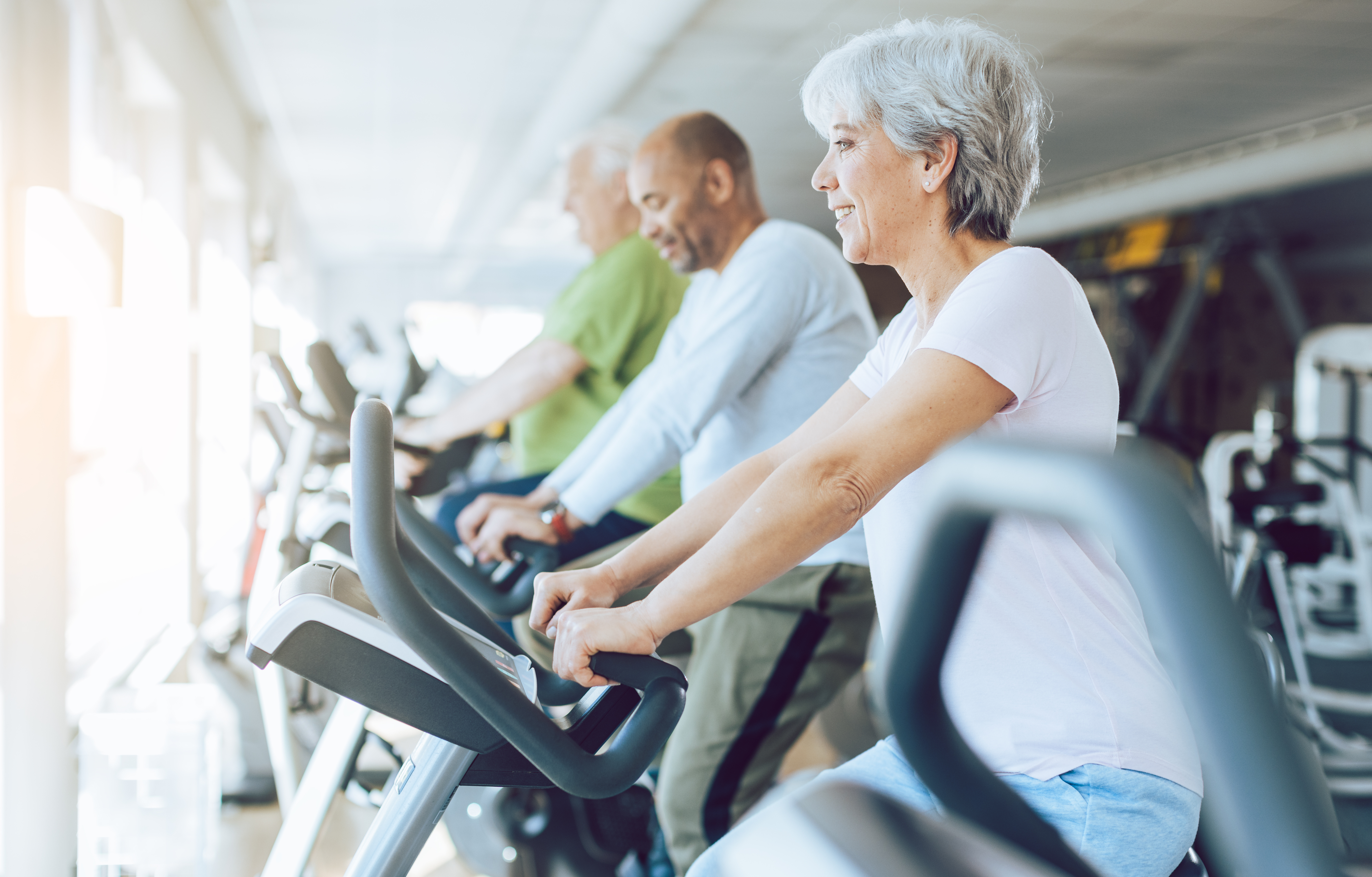 Fit seniors in diversity group on stationary fitness bikes in the gym