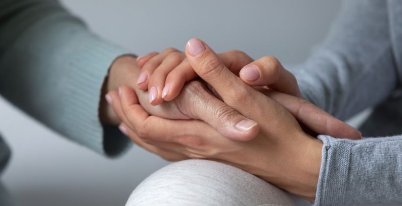 Caregiver and woman holding hands for comfort and concern
